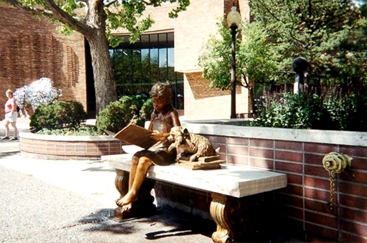 Girl statue reading with dog statue.