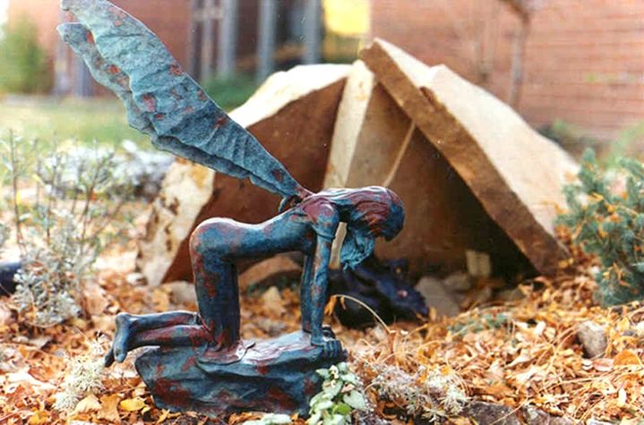 Fairy sculpture kneeling in garden setting.
