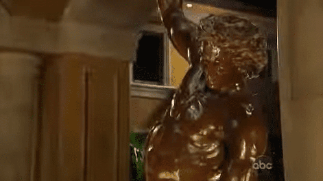 A golden statue of a muscular male figure holding something above his head indoors.